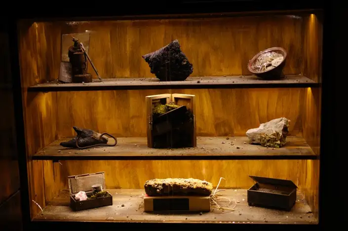 A lit wooden vitrine of objects recovered from the former camps, arranged across three shelves.