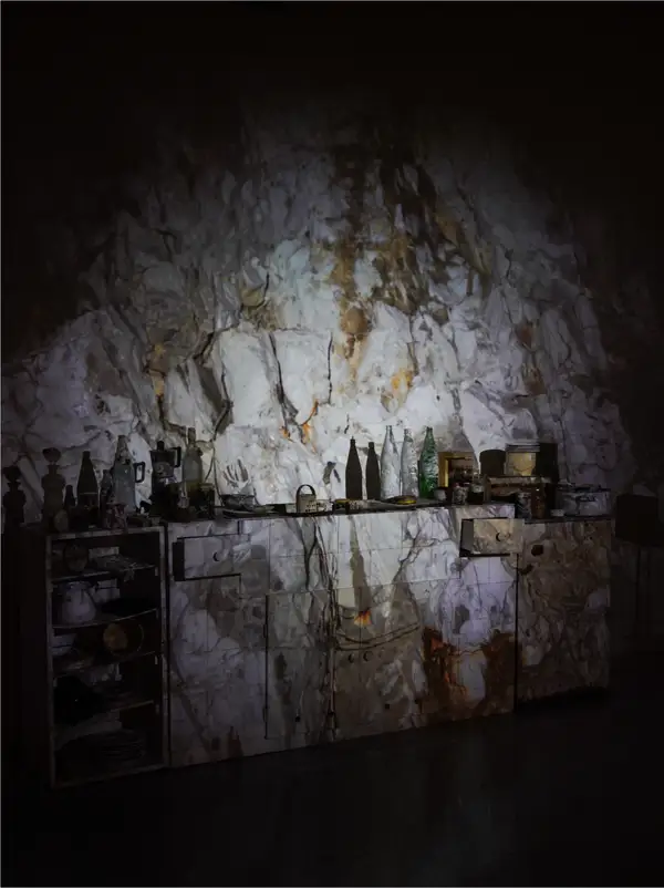 A kitchen dresser and shelves of crockery, a projection of pale rock face falling over the whole wall.